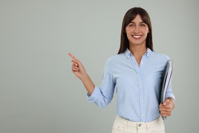 Happy secretary with folder pointing at something on light grey background. Space for text