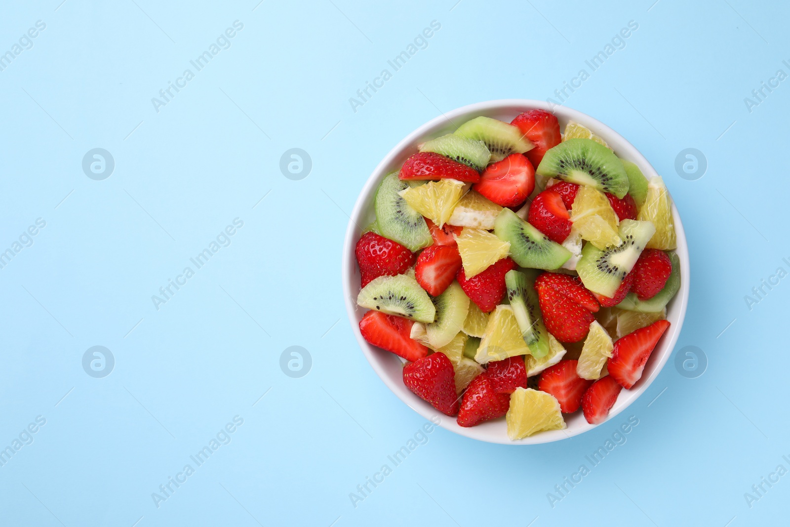 Photo of Yummy fruit salad in bowl on light blue background, top view. Space for text