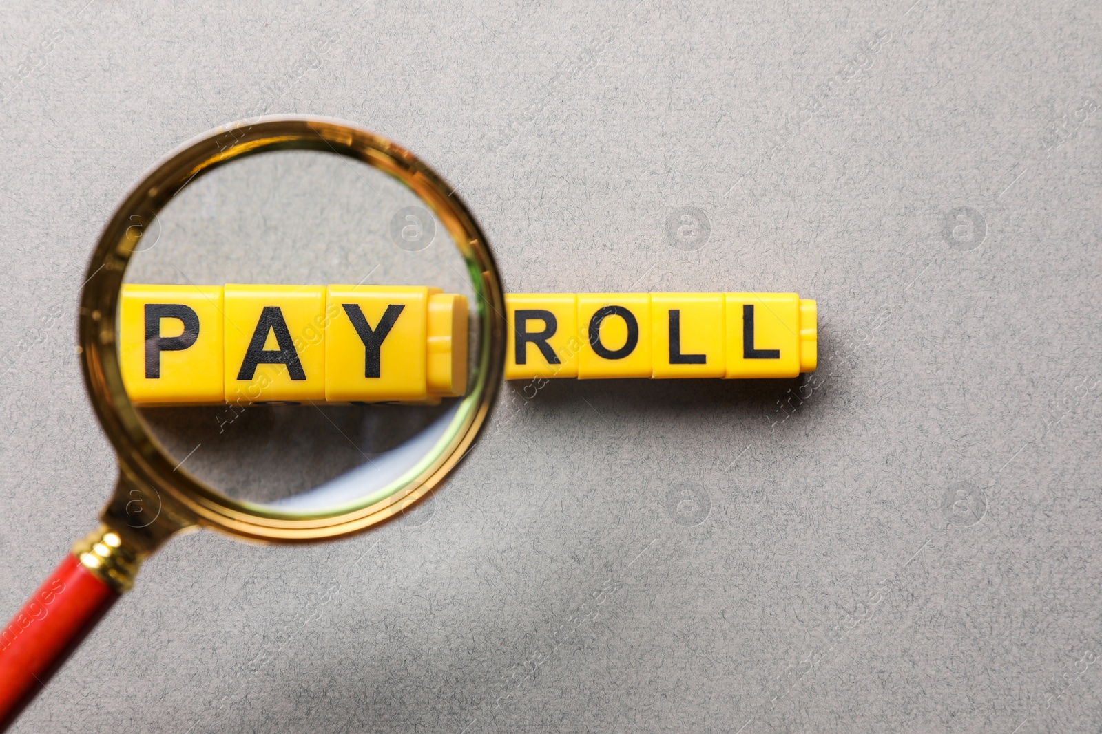 Photo of Word Payroll made with yellow cubes on light grey background, flat lay. View through magnifying glass