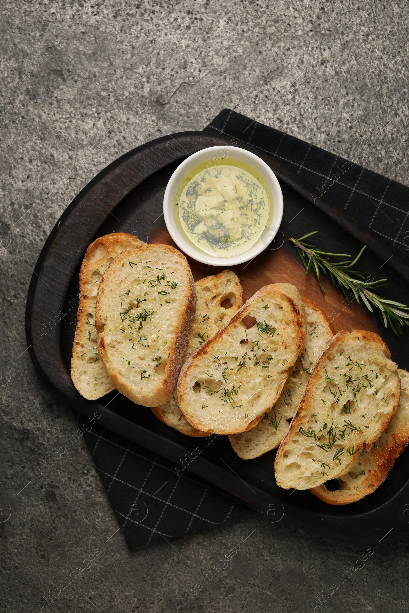 Photo of Tasty baguette with garlic and dill served on grey textured table, top view
