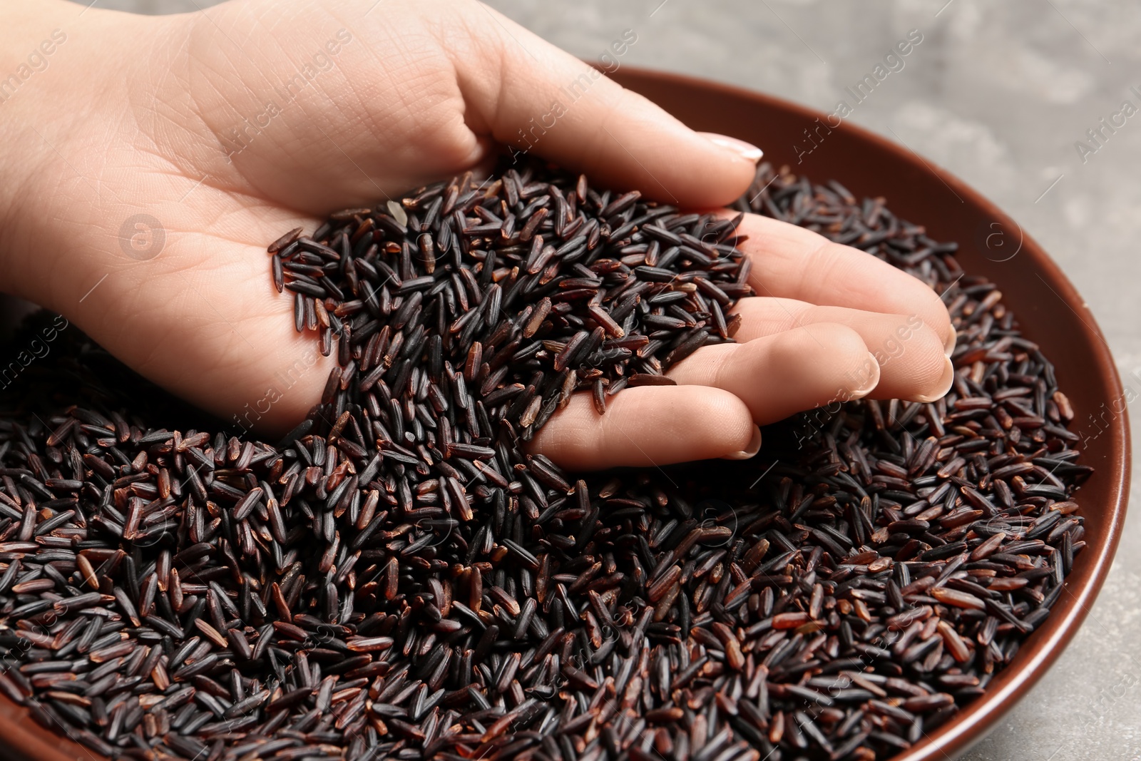 Photo of Woman holding grains near plate with black rice on table, closeup