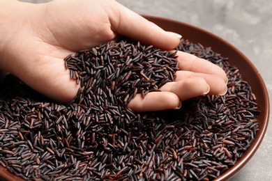 Photo of Woman holding grains near plate with black rice on table, closeup