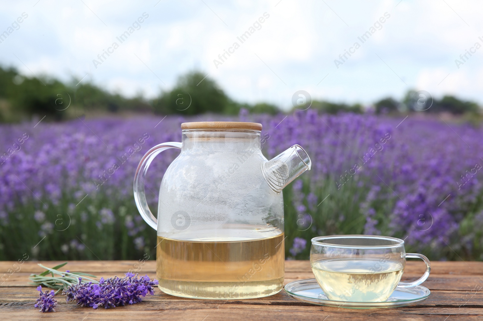 Photo of Tasty herbal tea and fresh lavender flowers on wooden table in field