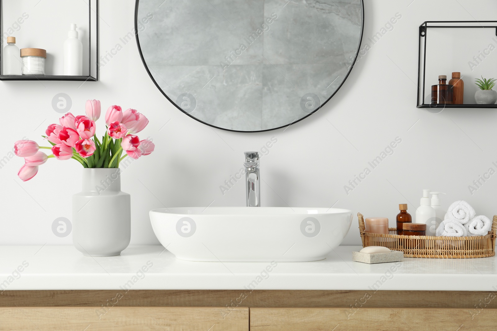 Photo of Vase with beautiful pink tulips and toiletries near sink in bathroom