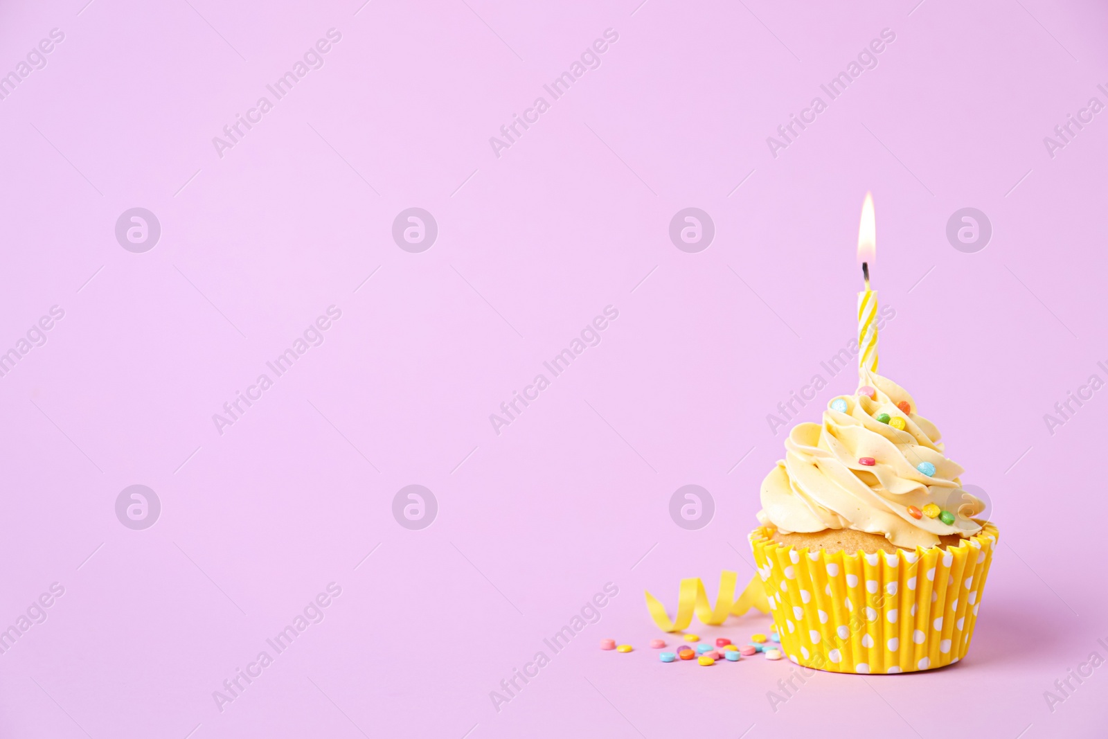 Photo of Delicious birthday cupcake with burning candle, sprinkles and streamer on pink background, space for text