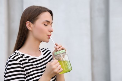 Photo of Young woman with mason jar of fresh juice outdoors, space for text