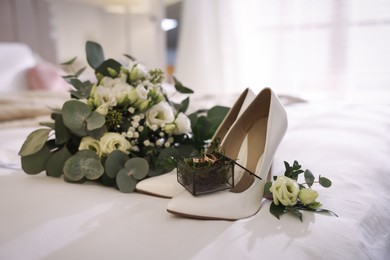 Beautiful wedding rings in glass box, bride's shoes and flowers on bed at home