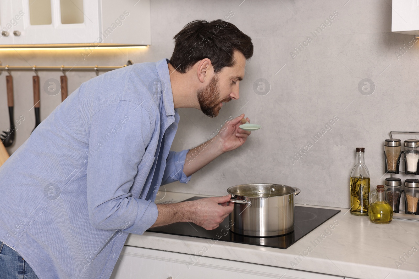 Photo of Man tasting delicious soup with spoon in kitchen