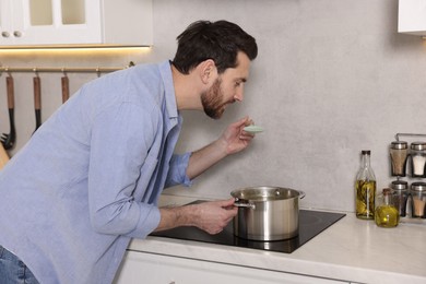 Man tasting delicious soup with spoon in kitchen