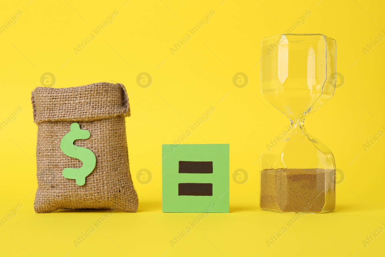 Photo of Burlap sack of money, hourglass with sand and equals sign on yellow background