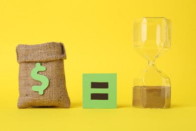 Burlap sack of money, hourglass with sand and equals sign on yellow background