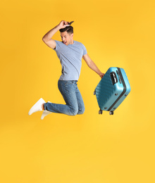 Photo of Handsome man with suitcase for summer trip jumping on yellow background. Vacation travel