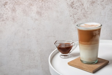 Glass of tasty caramel macchiato and gravy boat with syrup on table, space for text