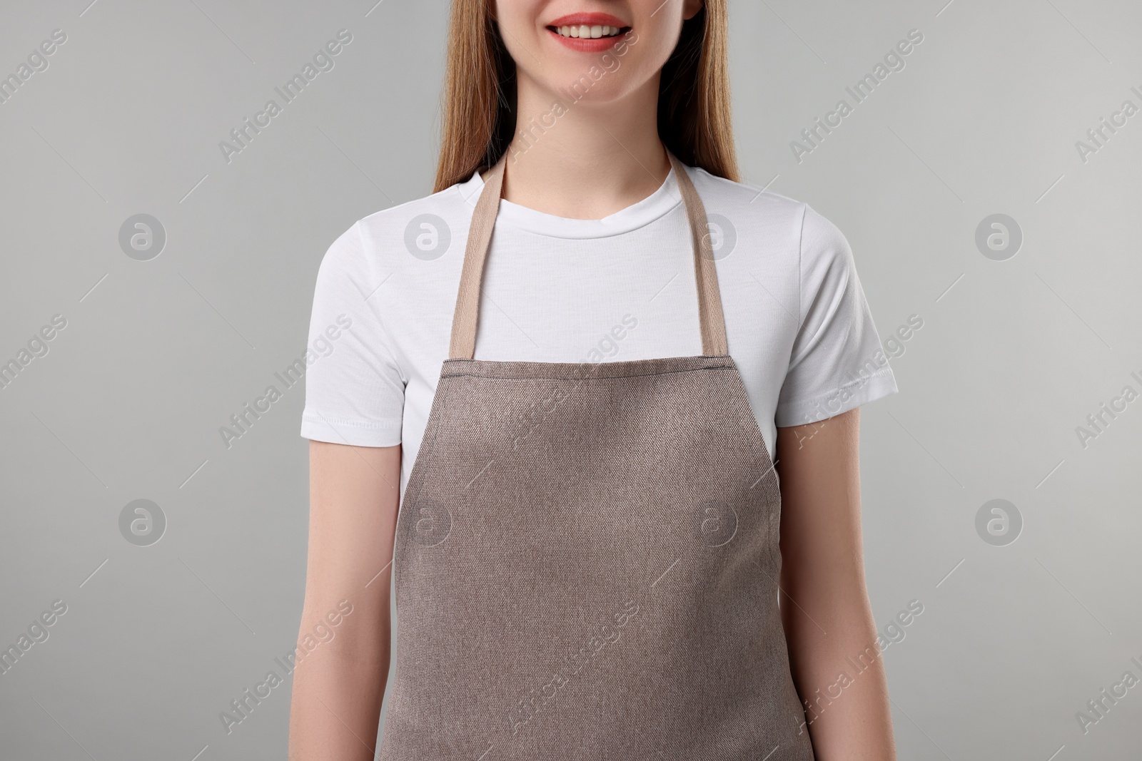 Photo of Woman wearing kitchen apron on grey background, closeup. Mockup for design