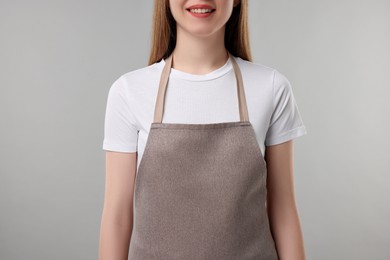 Photo of Woman wearing kitchen apron on grey background, closeup. Mockup for design