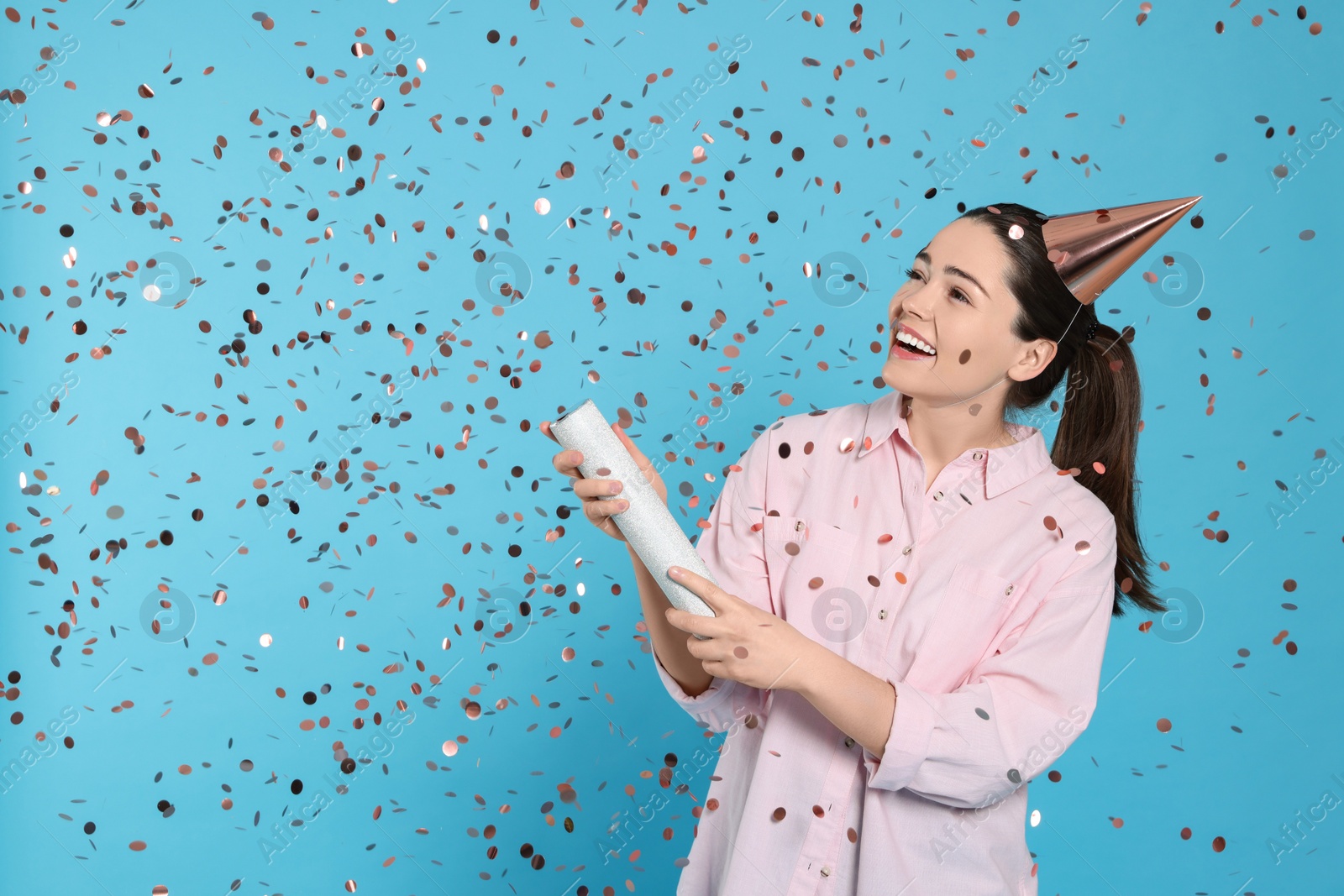 Photo of Young woman blowing up party popper on light blue background