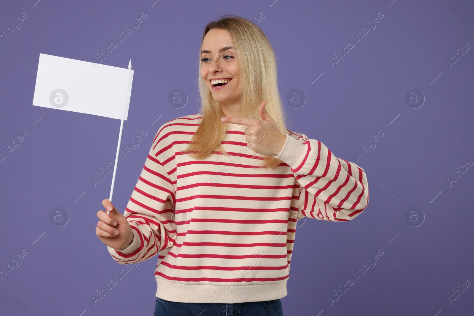 Photo of Happy woman pointing at blank white flag on violet background. Mockup for design