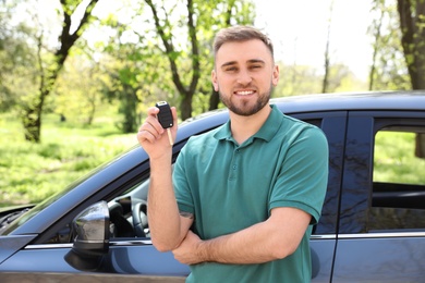 Young man with key near new car outdoors