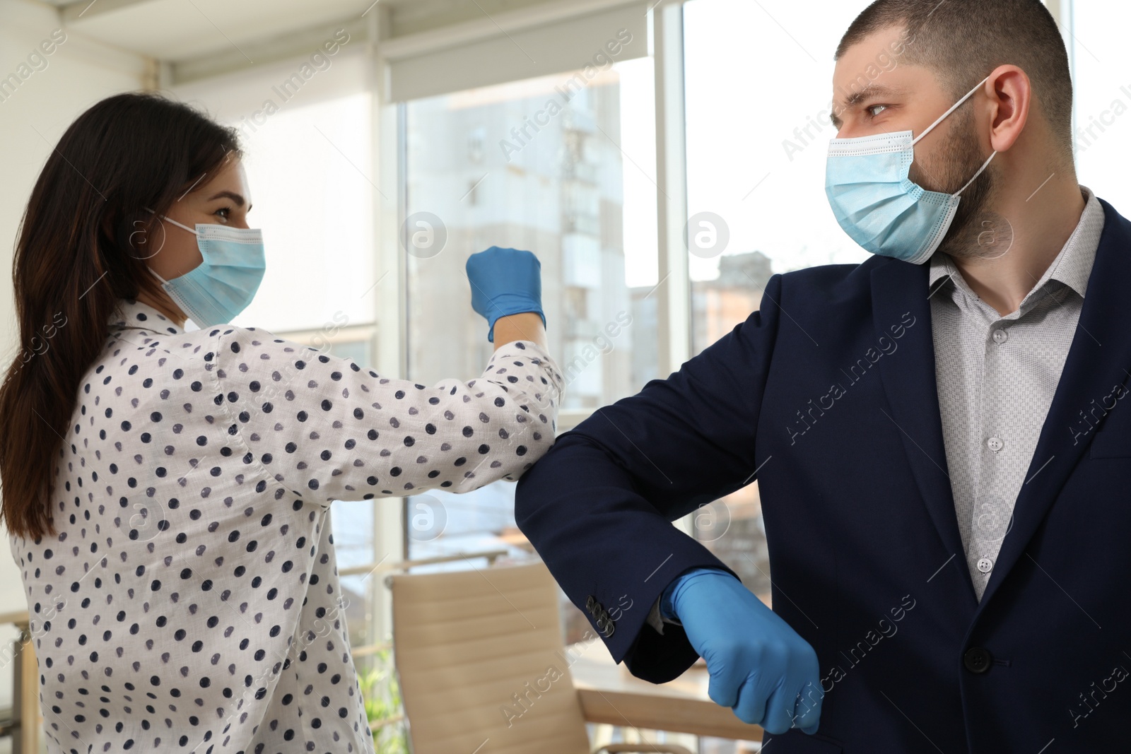 Photo of Office employees in masks greeting each other by bumping elbows at workplace