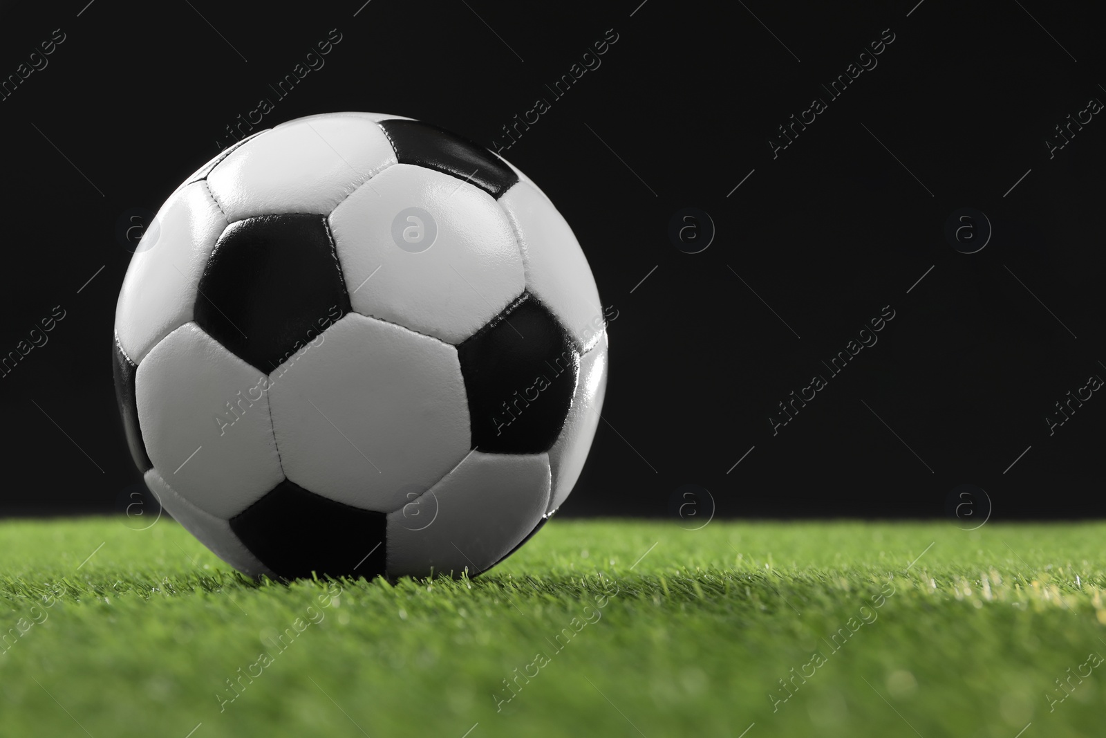 Photo of Soccer ball on green grass against black background, space for text