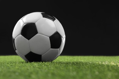 Photo of Soccer ball on green grass against black background, space for text