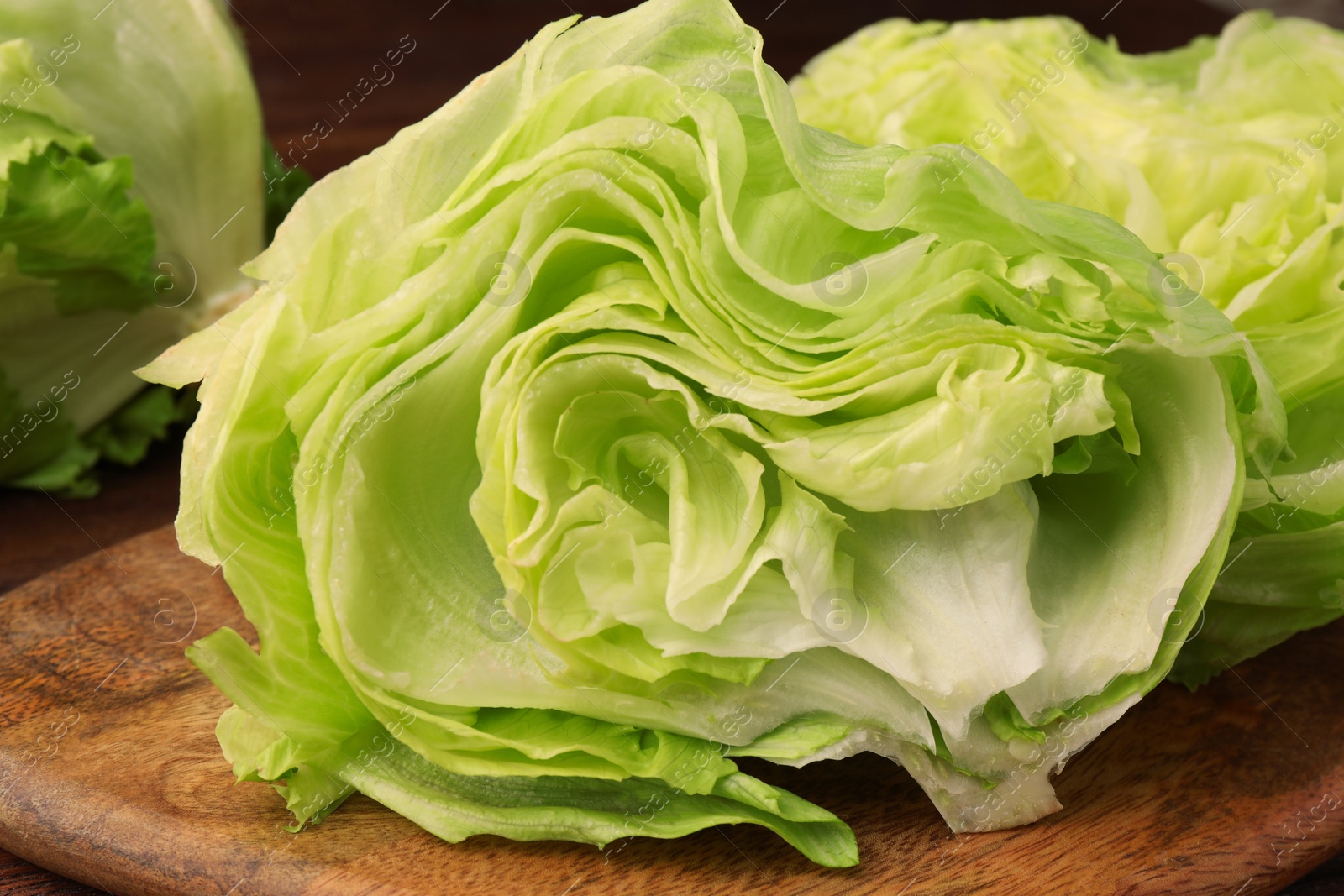 Photo of Board with halves of fresh green iceberg lettuce head on wooden table, closeup