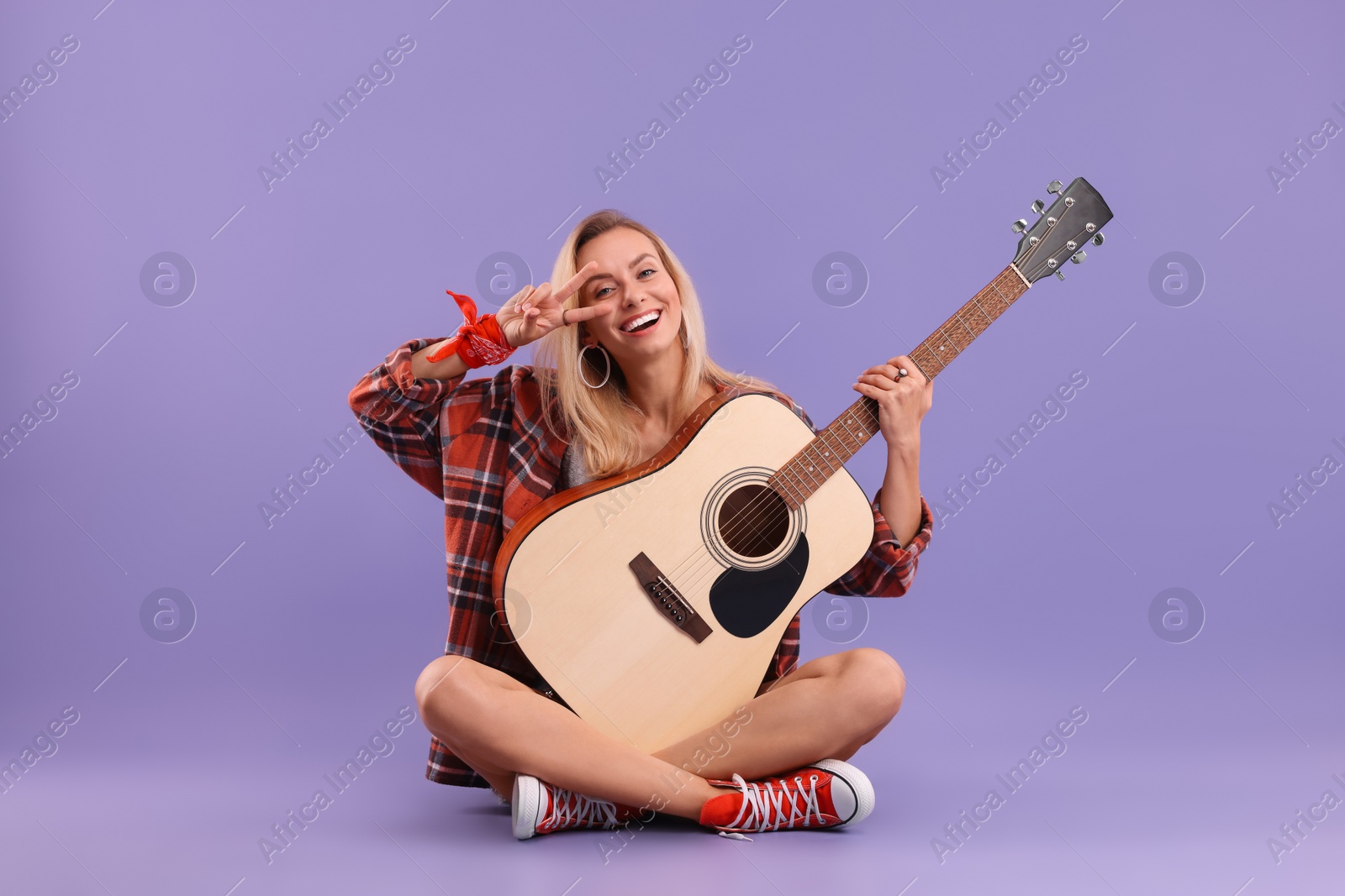 Photo of Happy hippie woman with guitar showing peace sign on purple background