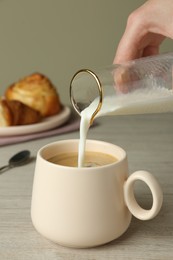 Woman pouring milk into cup of coffee at wooden table, closeup