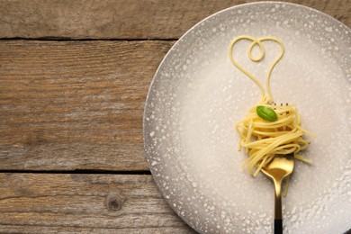 Heart made with spaghetti and fork on wooden table, top view. Space for text