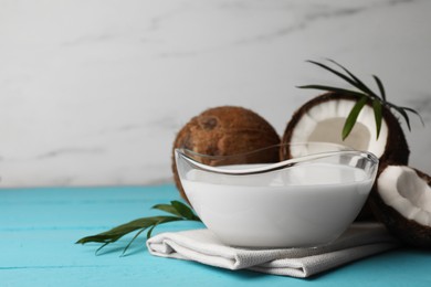 Photo of Bowl of delicious vegan milk, palm leaves and coconuts on light blue wooden table. Space for text
