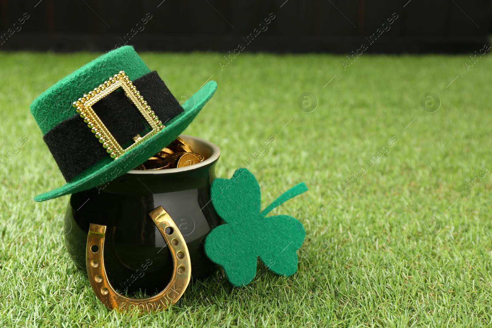 Photo of St. Patrick's day. Pot of gold with leprechaun hat, horseshoe and decorative clover leaf on green grass. Space for text