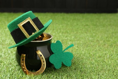 St. Patrick's day. Pot of gold with leprechaun hat, horseshoe and decorative clover leaf on green grass. Space for text