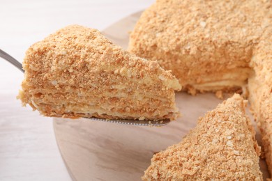 Taking piece of delicious Napoleon cake from table, closeup