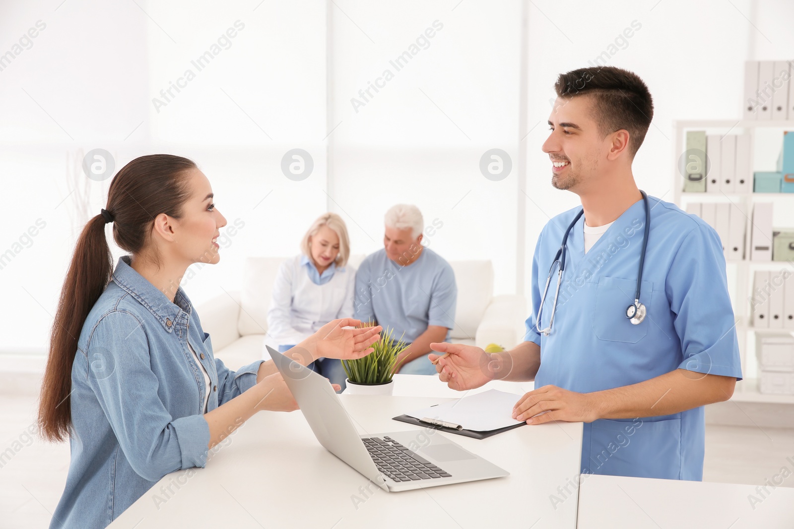 Photo of Young male doctor working with client at reception desk in hospital