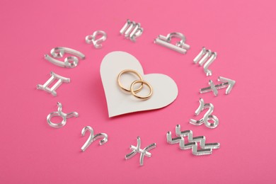 Photo of Zodiac signs, heart and wedding rings on pink background