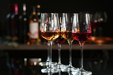 Glasses with different wines on bar counter against blurred background. Space for text