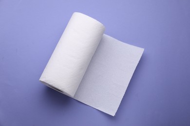 Photo of Roll of tissue towels on violet background, top view