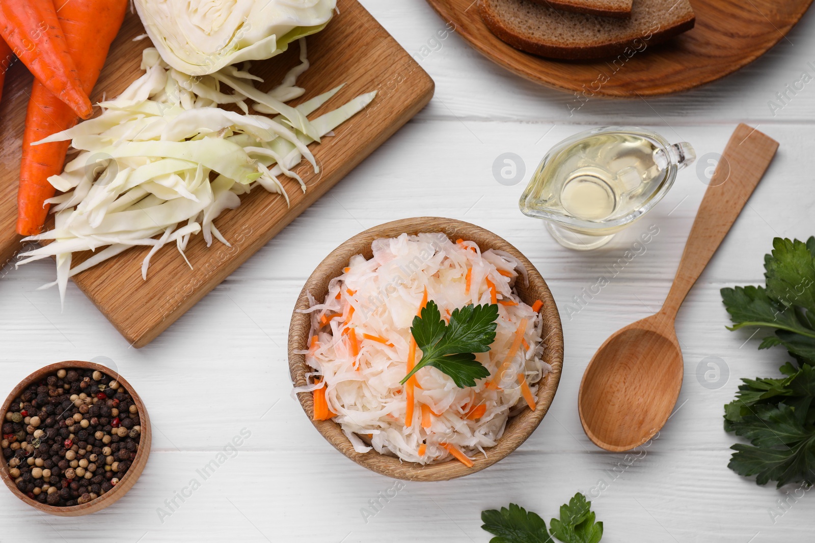 Photo of Bowl of tasty sauerkraut and ingredients on white wooden table, flat lay