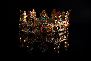 Photo of Beautiful golden crown with gems on dark mirror surface