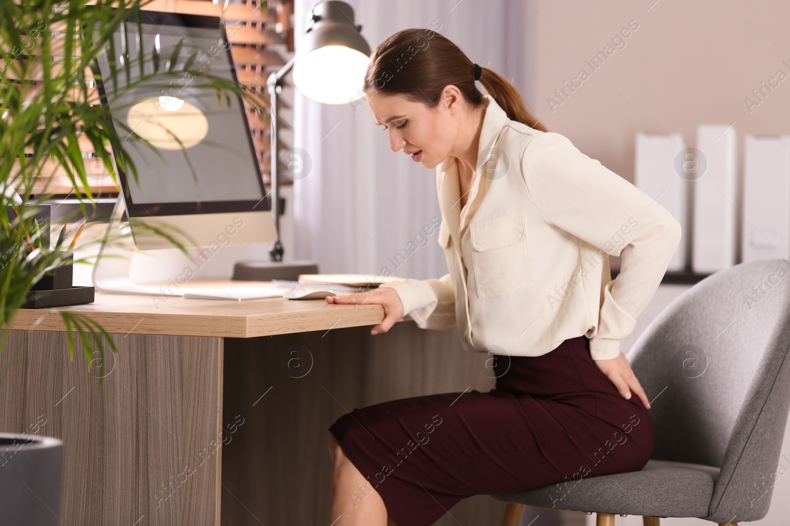 Photo of Young woman suffering from hemorrhoid at workplace in office