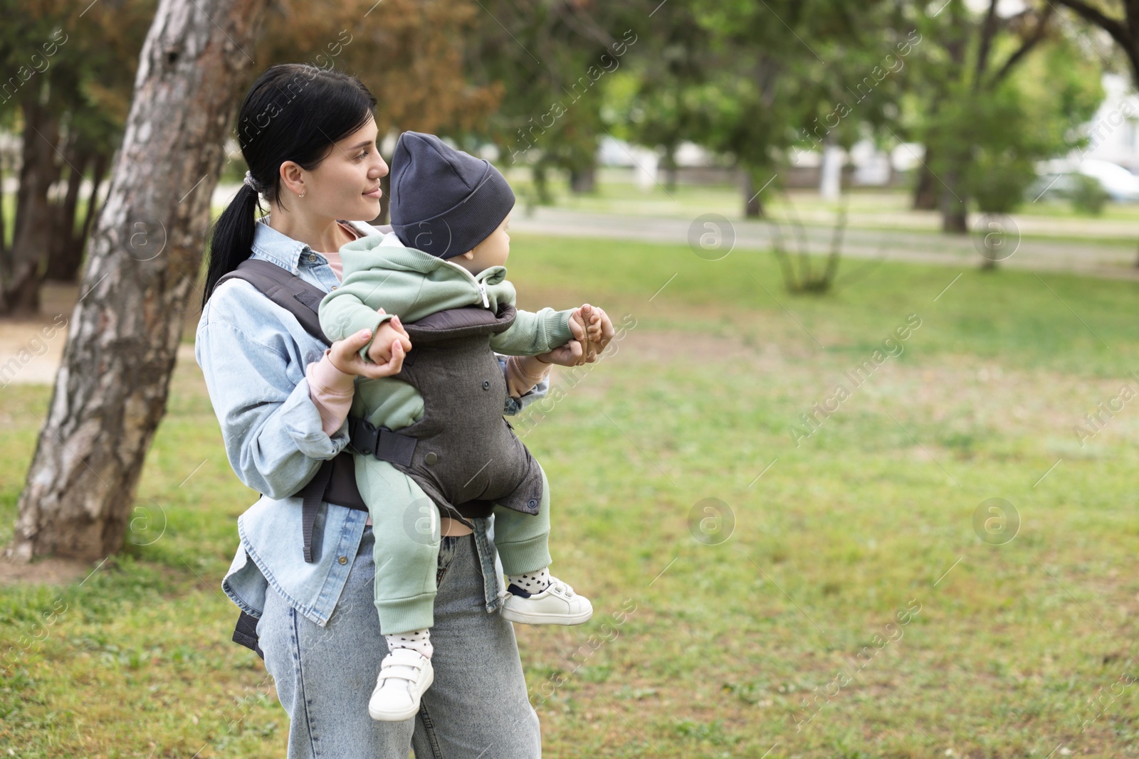 Photo of Mother holding her child in sling (baby carrier) in park. Space for text