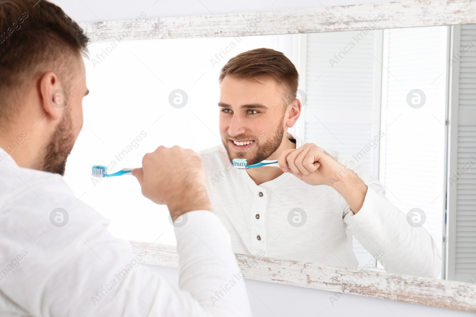 Photo of Young man cleaning teeth against mirror in bathroom