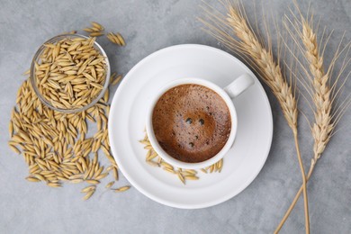 Cup of barley coffee, grains and spikes on gray table, flat lay