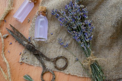 Photo of Beautiful lavender flowers, bottles of essential oil and scissors on wooden table, flat lay