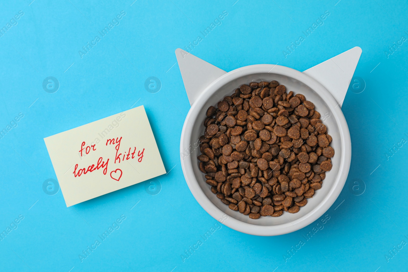 Photo of Feeding bowl of kibble with cat ears and cute note For My Lovely Kitty on light blue background, flat lay