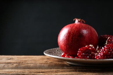 Photo of Plate with ripe pomegranates on table against black background, space for text