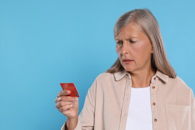 Worried woman with credit card on light blue background, space for text. Be careful - fraud
