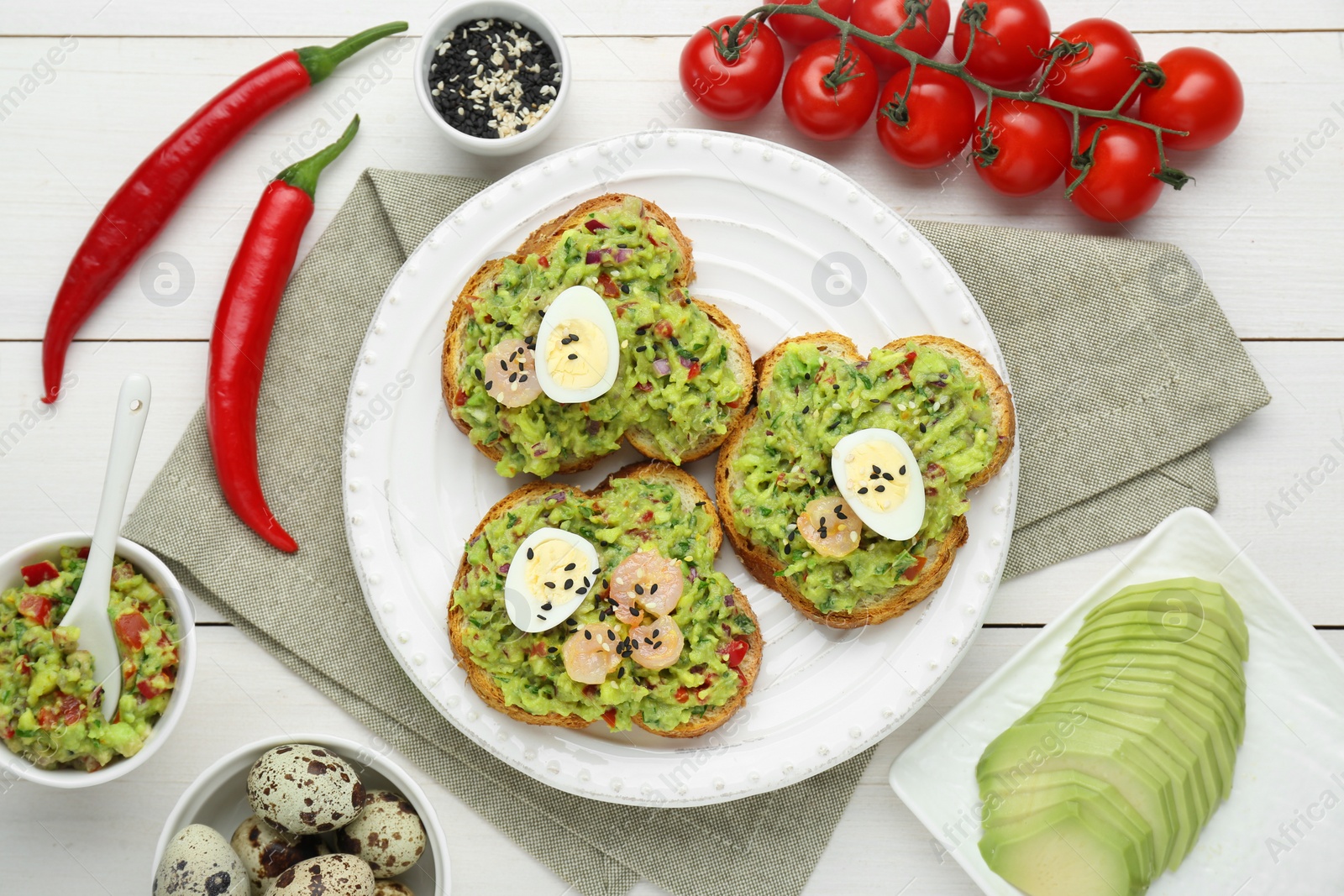 Photo of Slices of bread with tasty guacamole, eggs, shrimp and ingredients on white wooden table, flat lay