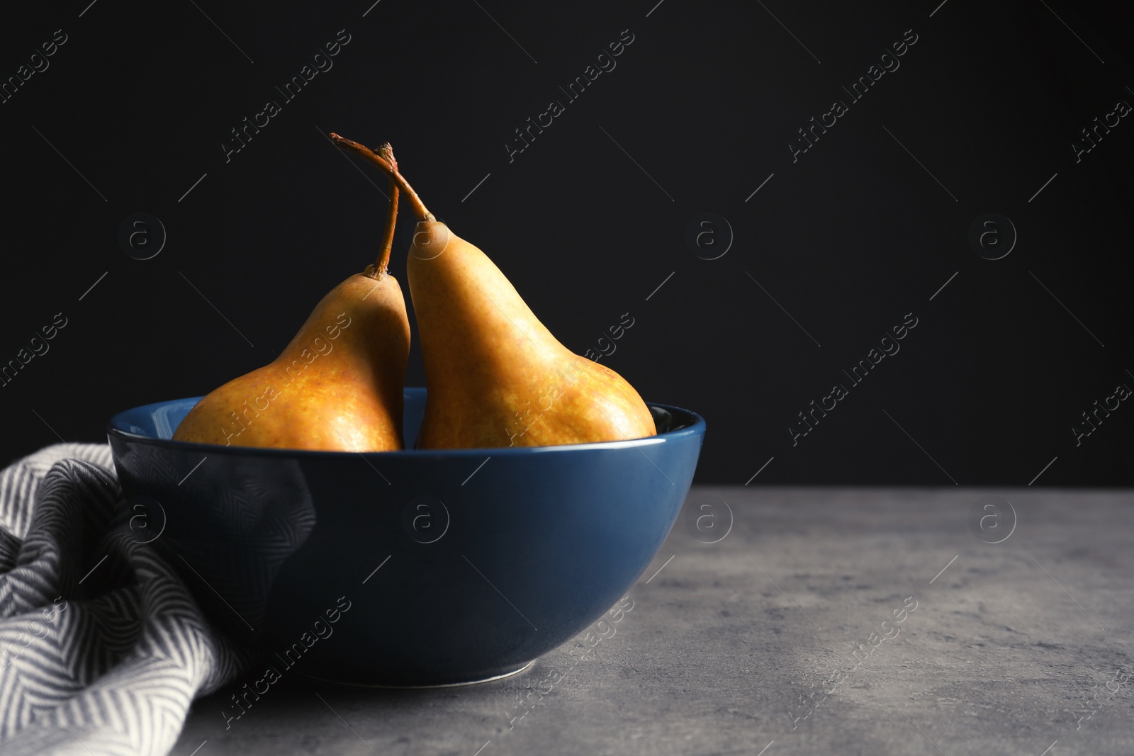 Photo of Bowl with ripe pears on table against black background. Space for text