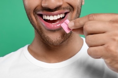 Photo of Happy man putting bubble gum into mouth on green background, closeup